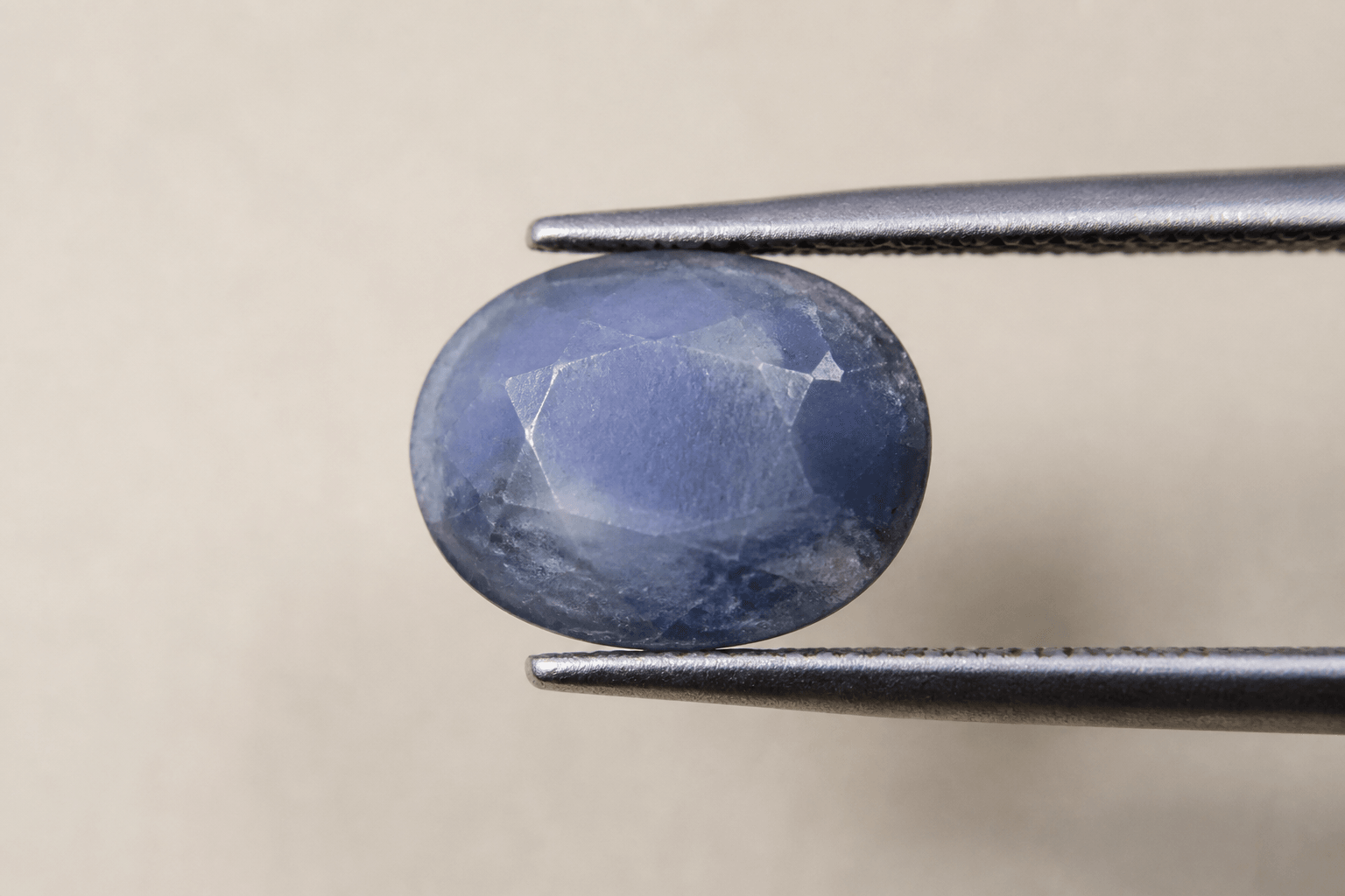 Dull, cloudy oval blue sapphire held in tweezers before restoration